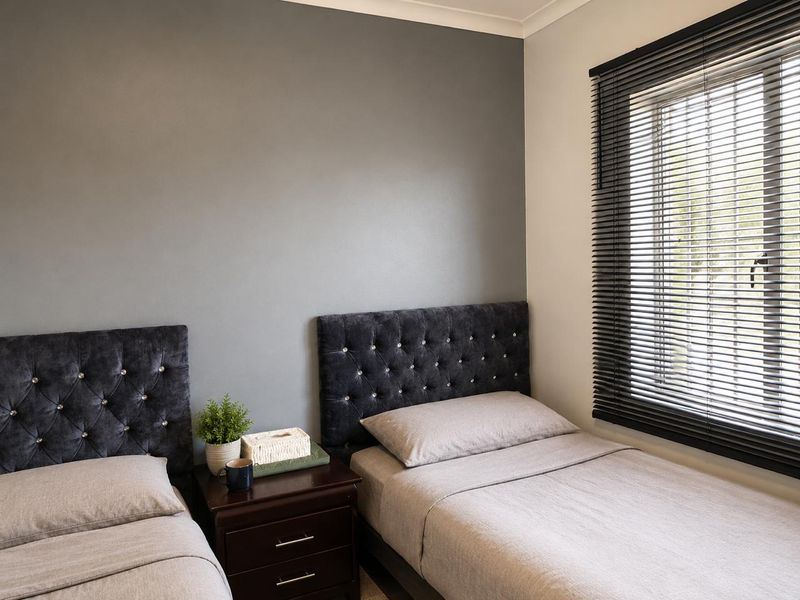 A well-maintained bedroom featuring a neutral grey accent wall, fitted venetian blinds, and classic coving detail.