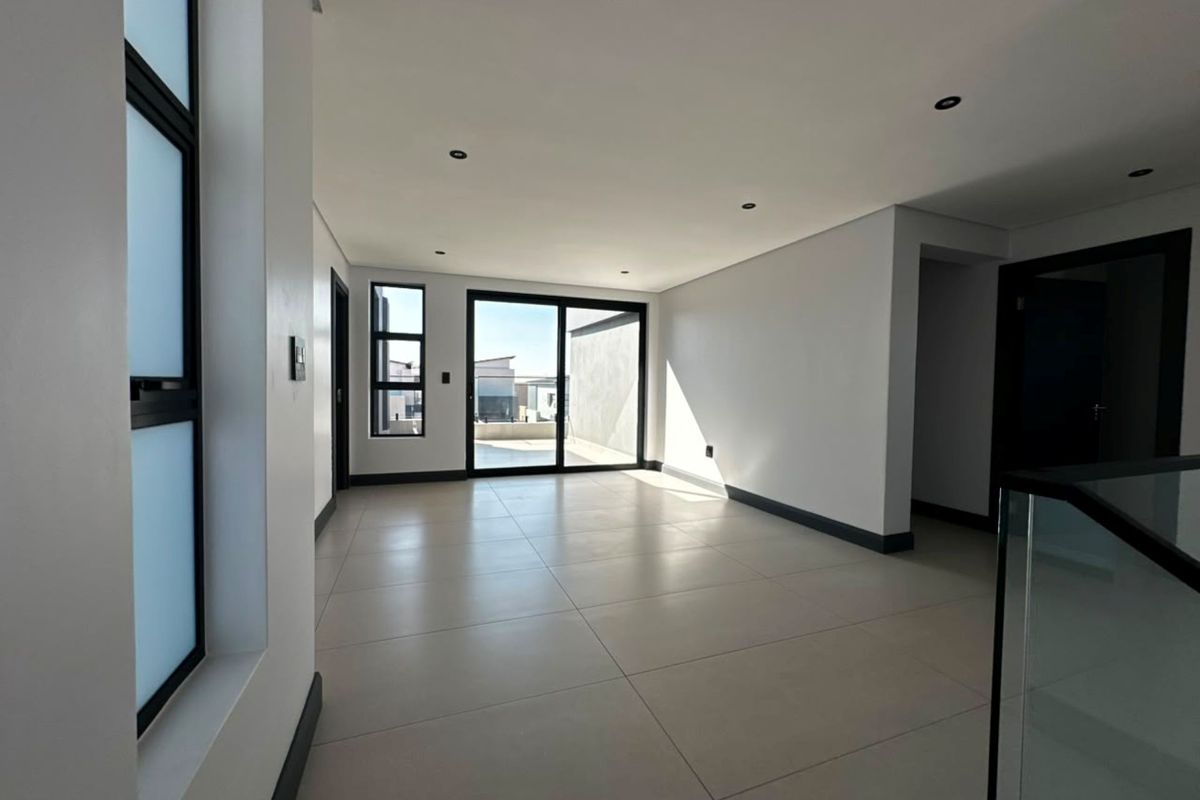 A bright, modern, and spacious open-plan living area featuring large format floor tiles, recessed lighting, and sliding glass doors leading to an outdoor space.