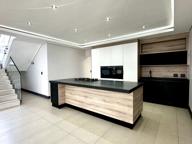 Modern open-plan kitchen featuring a central island, built-in appliances, sleek cabinetry, and an adjacent staircase with a contemporary glass balustrade.