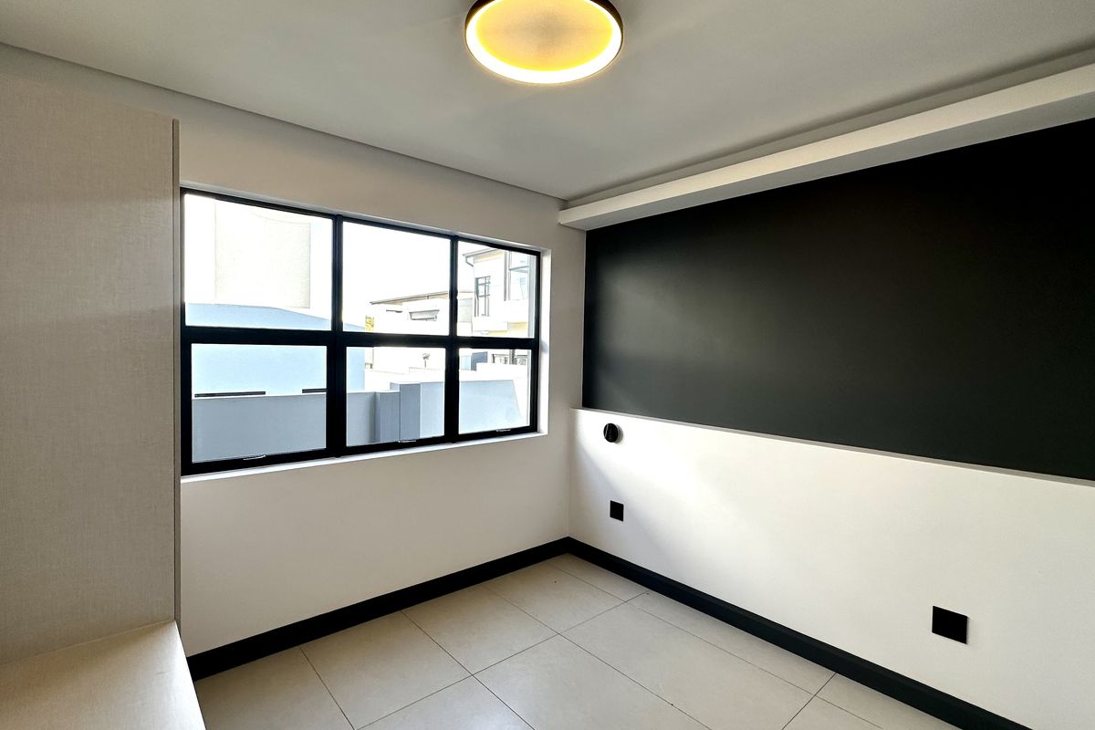 A modern, empty bedroom featuring neutral tiled flooring, built-in cabinetry, and a striking black accent wall with large windows providing natural light.