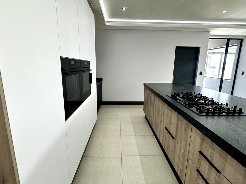 Modern kitchen featuring a large island with a gas hob, built-in oven, sleek cabinetry, and recessed ceiling lighting in a clean, contemporary space.