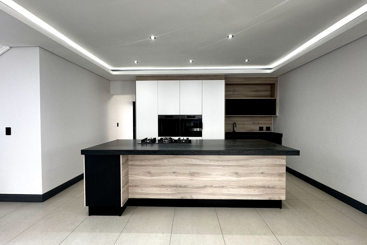 Modern kitchen featuring a central island with a gas hob, built-in ovens, sleek cabinetry, and recessed ceiling lighting in a clean, contemporary space.