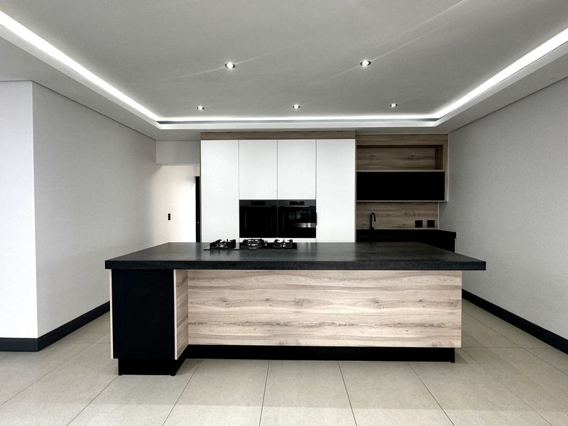 Modern kitchen featuring a central island with a gas hob, built-in ovens, sleek cabinetry, and recessed ceiling lighting in a clean, contemporary space.