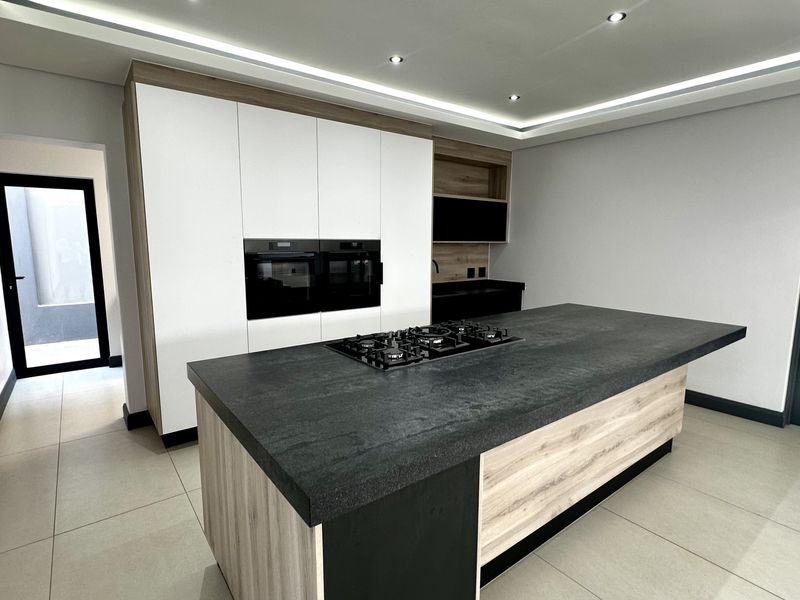 Modern kitchen featuring a large central island with a gas hob, built-in ovens, sleek cabinetry, and recessed ceiling lighting.