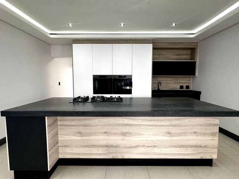 Modern kitchen featuring a large central island with a built-in gas hob, integrated ovens, and sleek contemporary cabinetry with recessed ceiling lighting.