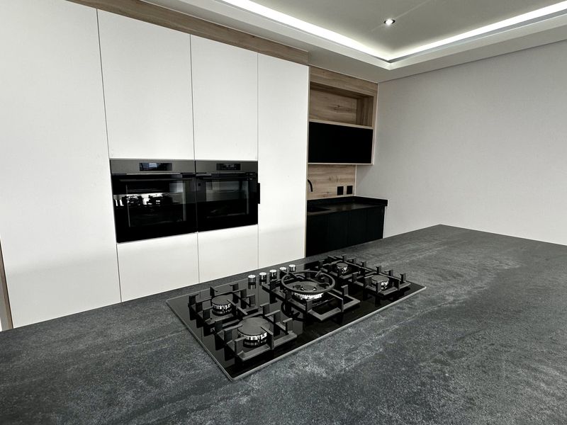 Modern kitchen featuring a large island with a built-in gas cooktop, sleek cabinetry, and integrated double ovens in a contemporary design.