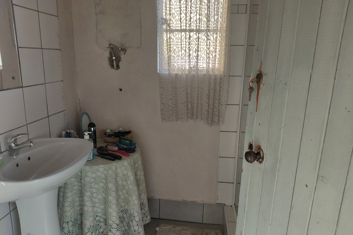 A small bathroom featuring a pedestal basin and tiled finishes, currently requiring maintenance and cosmetic updates to the walls and door.