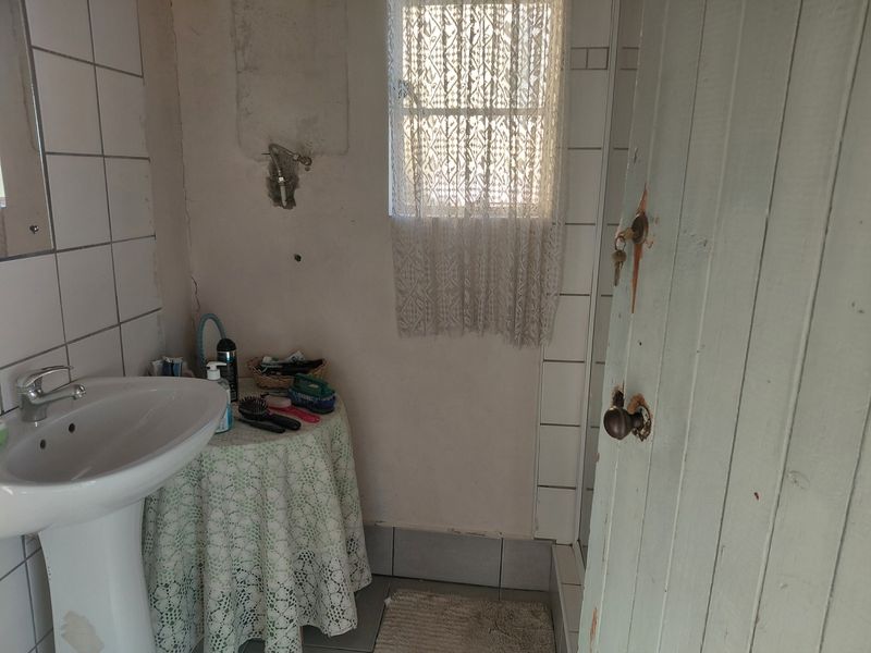 A small bathroom featuring a pedestal basin and tiled finishes, currently requiring maintenance and cosmetic updates to the walls and door.
