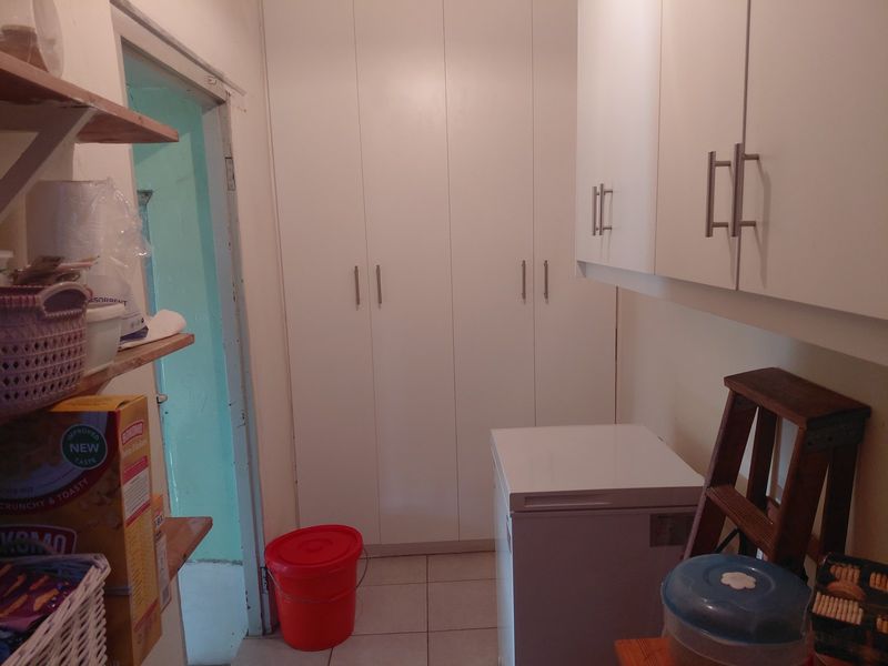 A functional scullery or pantry area featuring white built-in cabinetry and tiled flooring, providing additional storage space adjacent to the main kitchen.
