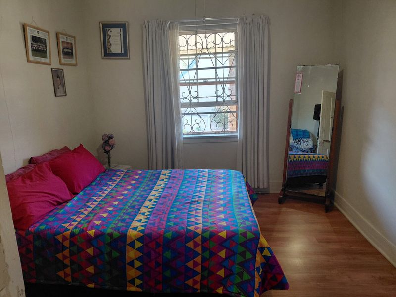 A standard bedroom featuring laminate flooring, a window with security bars, and neutral wall finishes.