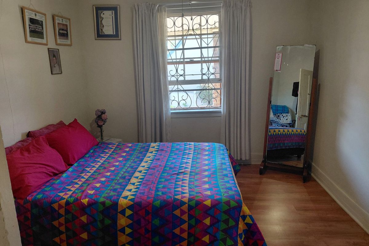 A standard bedroom featuring laminate flooring, a window with security bars, and neutral wall finishes.