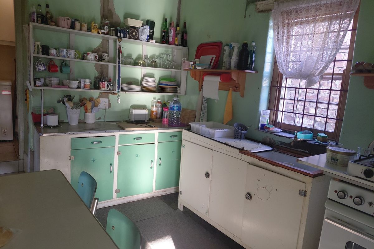 A dated kitchen featuring original cabinetry, a sink, and a freestanding stove, requiring significant renovation and cosmetic updates to improve functionality and aesthetic appeal.