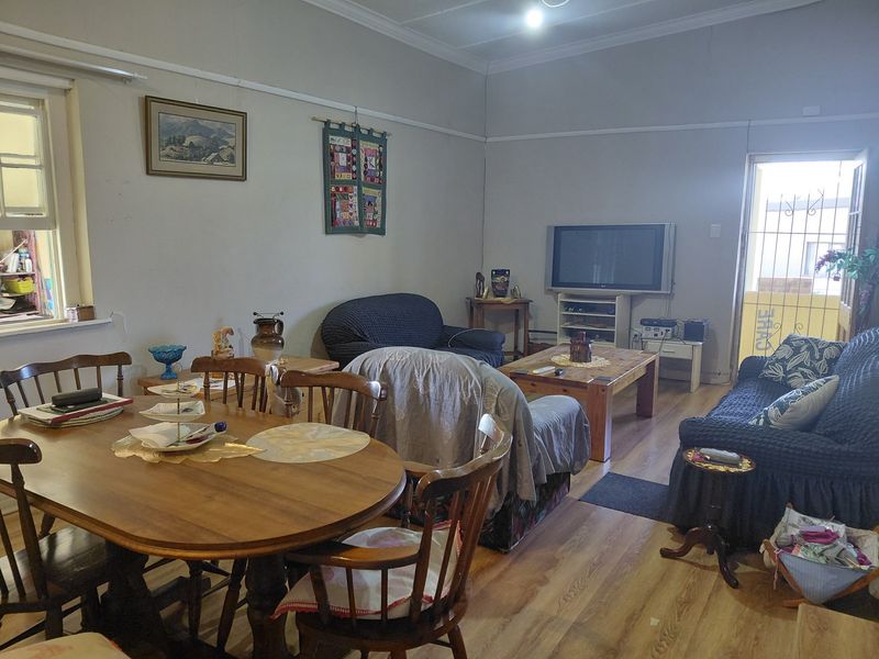 Open-plan living and dining area featuring laminate flooring, coved ceilings, and access to an exterior space via a security gate.