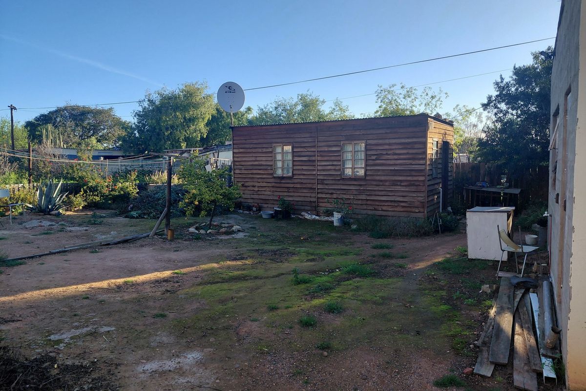A rear garden view featuring a detached timber-clad outbuilding with a corrugated metal roof and a satellite dish installed.