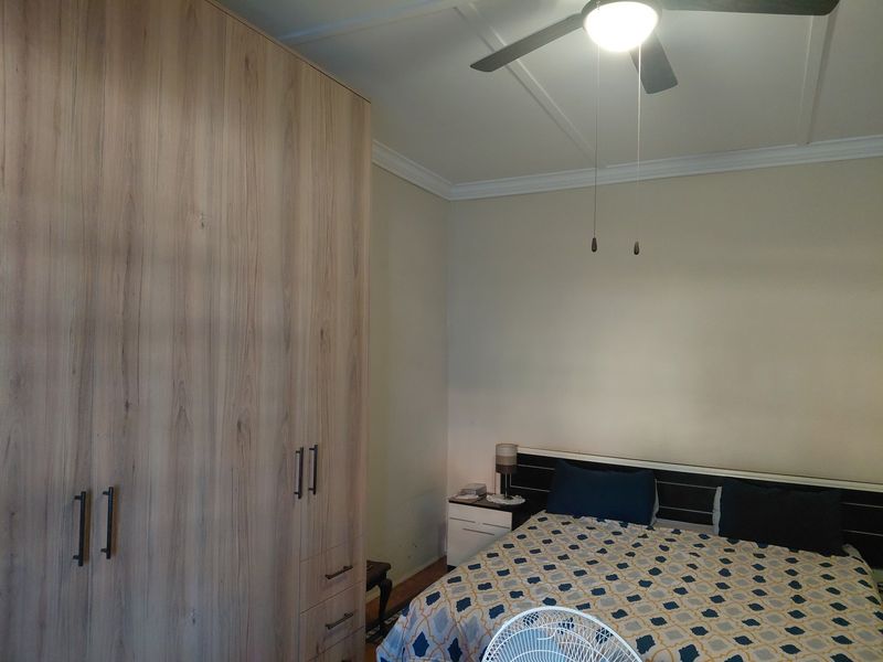A well-maintained bedroom featuring a large built-in wardrobe, crown molding, and a ceiling fan.