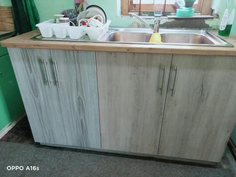 A kitchen sink area featuring wood-look cabinetry, a stainless steel double sink, and a wooden countertop, requiring minor wall repairs.
