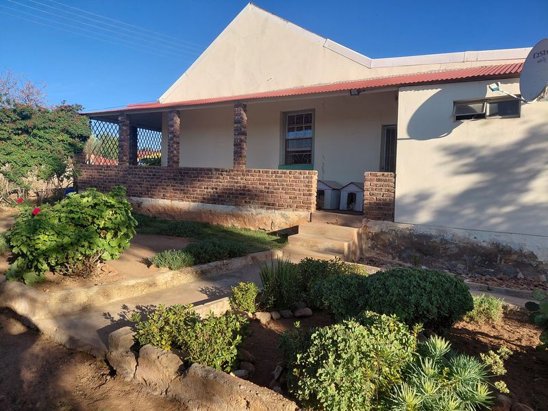Front elevation of a house featuring a brick veranda, covered porch area, and established garden with a concrete pathway leading to the entrance.