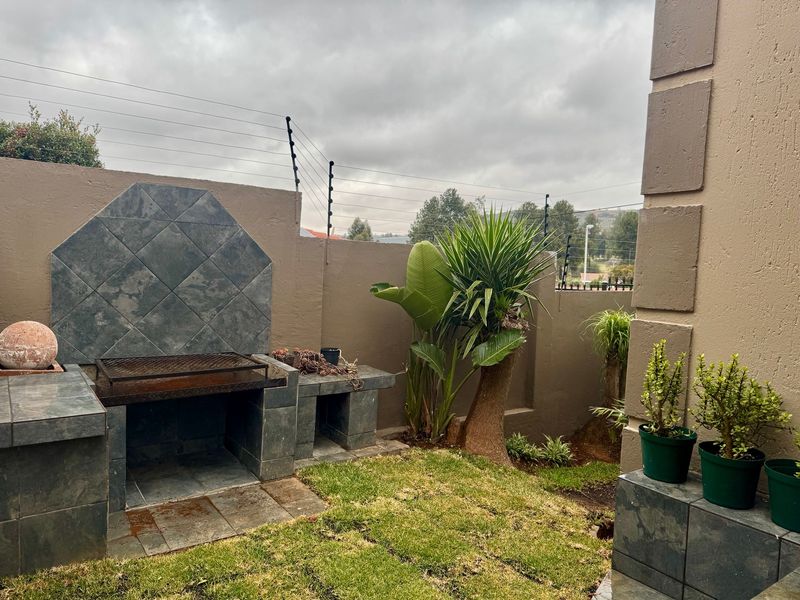 Outdoor patio area featuring a built-in tiled braai, perimeter wall with electric fencing, and a small garden space.