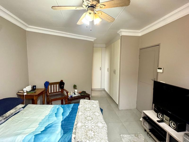 A bedroom featuring tiled flooring, built-in cupboards, and a ceiling fan, offering a functional space with neutral wall tones.