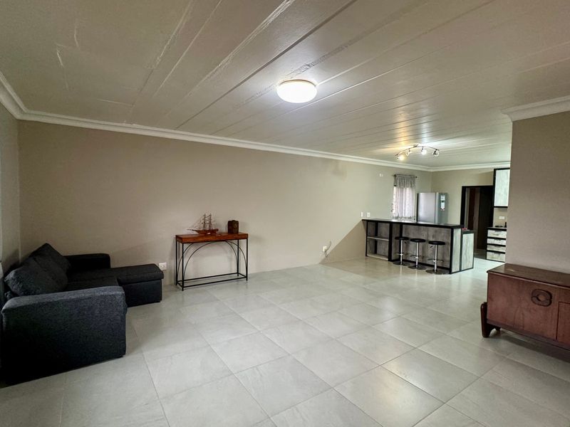Spacious open-plan living area featuring large format floor tiles, a breakfast bar, and a functional kitchen layout with built-in cabinetry.