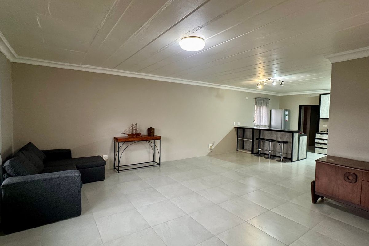 Spacious open-plan living area featuring large format floor tiles, a breakfast bar, and a functional kitchen layout with built-in cabinetry.