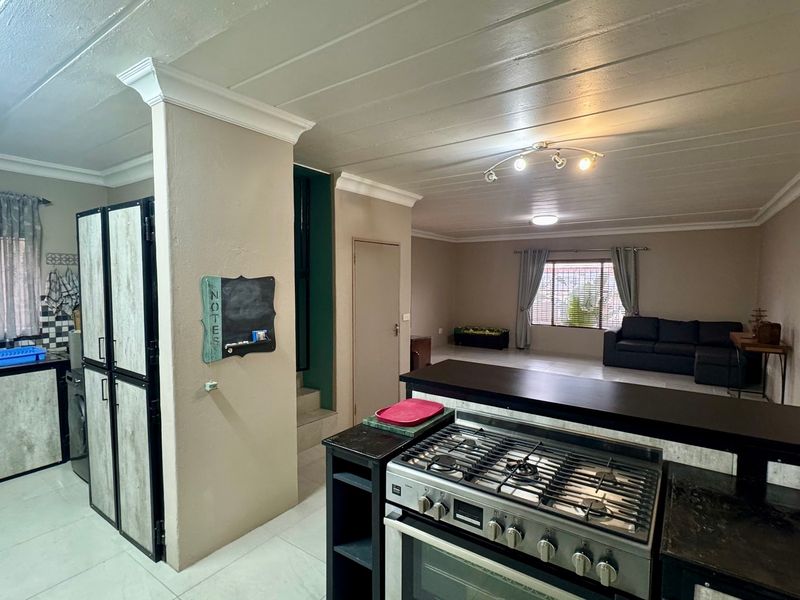 Open-plan living area featuring a kitchen with a gas stove, breakfast bar, and tiled flooring, flowing into a spacious lounge area.