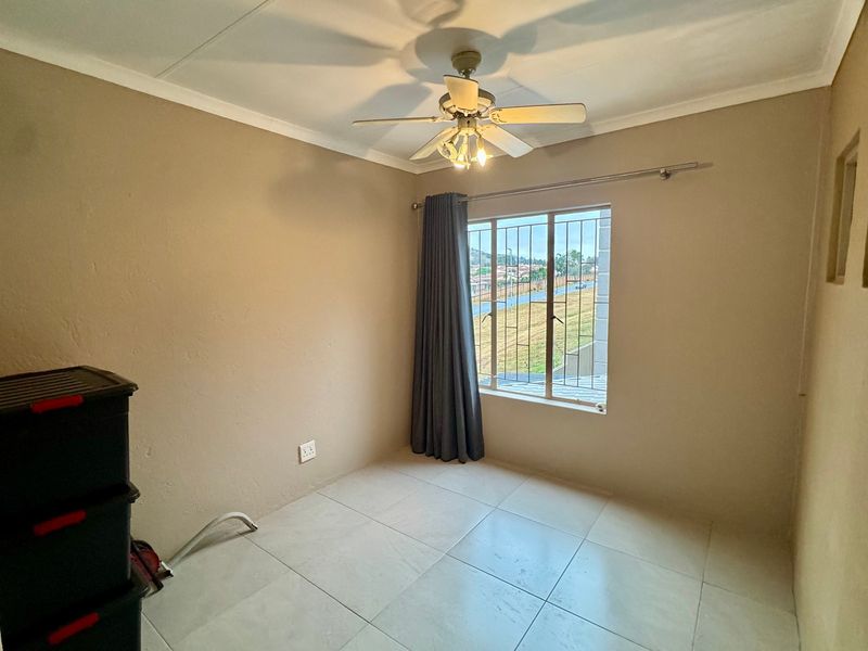 A bright, empty bedroom featuring tiled flooring, a ceiling fan, and a window fitted with security bars.
