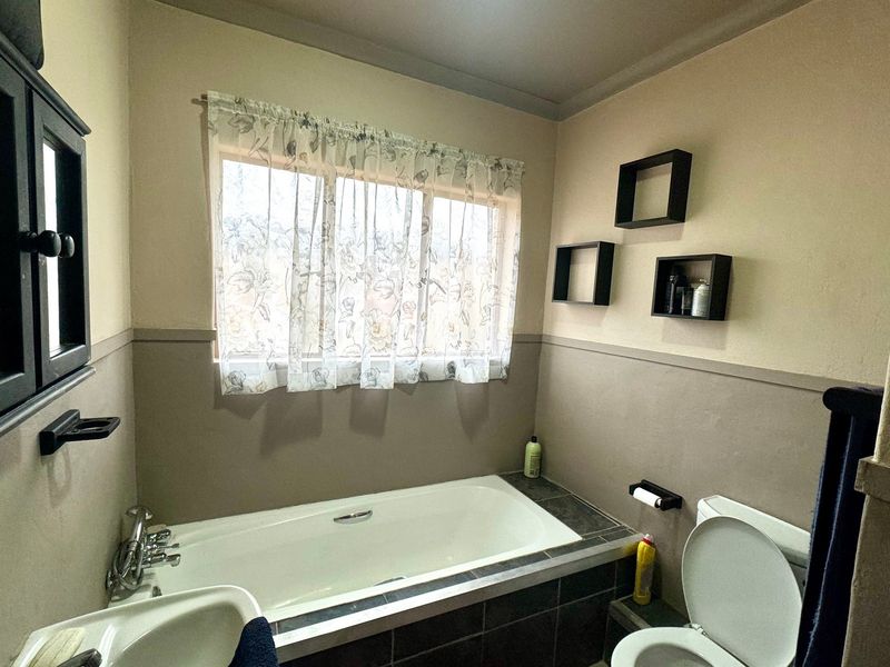 A functional bathroom featuring a built-in bathtub with tiled surround, a standard toilet, and a basin, finished with neutral wall tones.