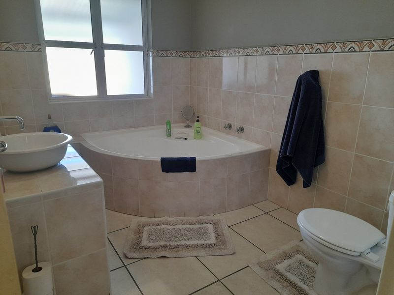 A functional bathroom featuring a corner bathtub, tiled vanity with a vessel sink, and a wall-mounted toilet with neutral ceramic tiling.