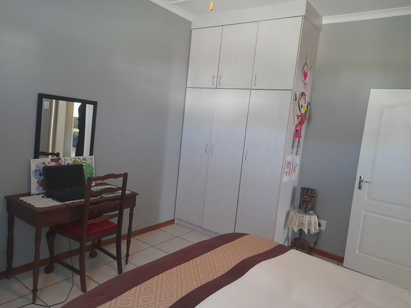 A bedroom featuring neutral grey walls, tiled flooring, and a large white built-in wardrobe providing ample storage space.