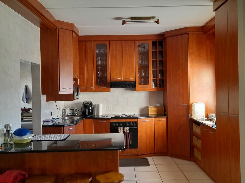A functional kitchen featuring warm-toned wooden cabinetry, granite countertops, a built-in oven with hob, and a convenient breakfast nook area.