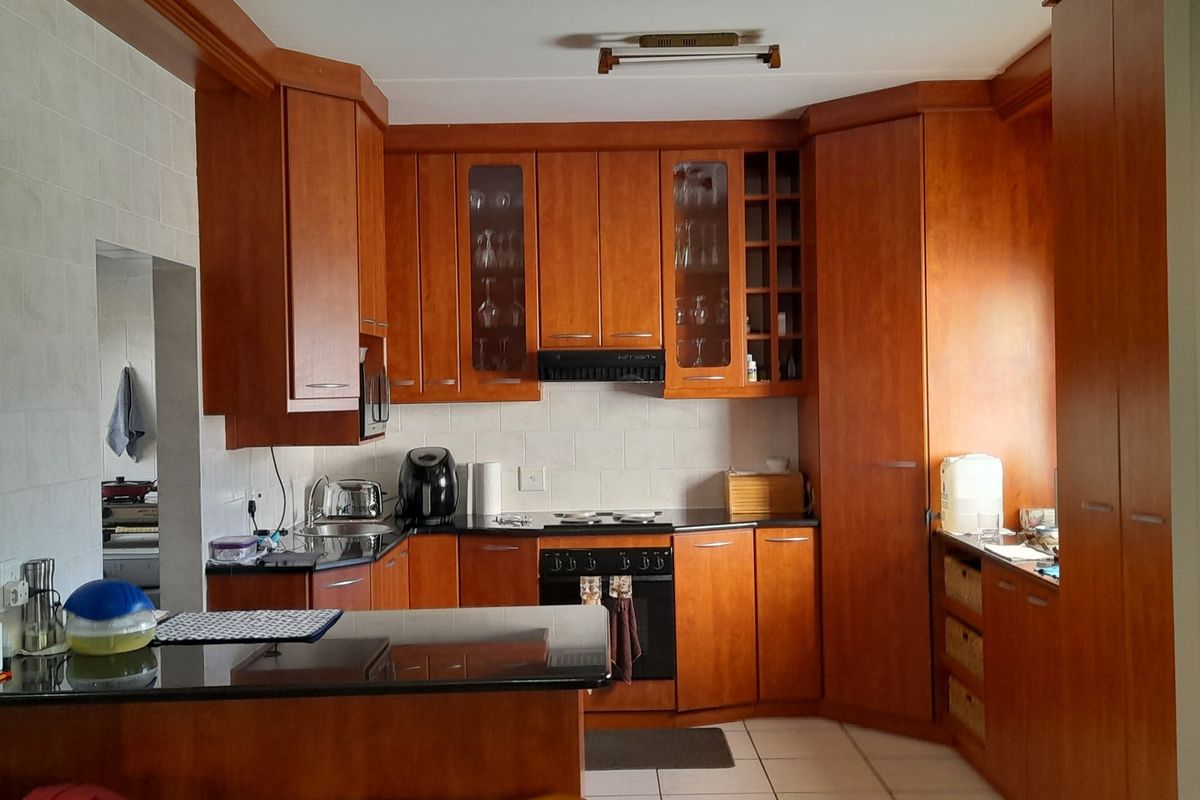A functional kitchen featuring warm-toned wooden cabinetry, granite countertops, a built-in oven with hob, and a convenient breakfast nook area.