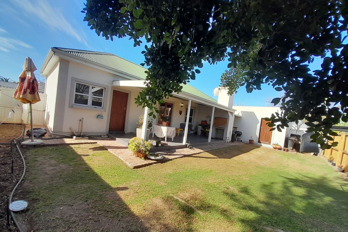 Rear view of the house featuring a covered patio with a built-in braai, brick paved area, and a private garden.