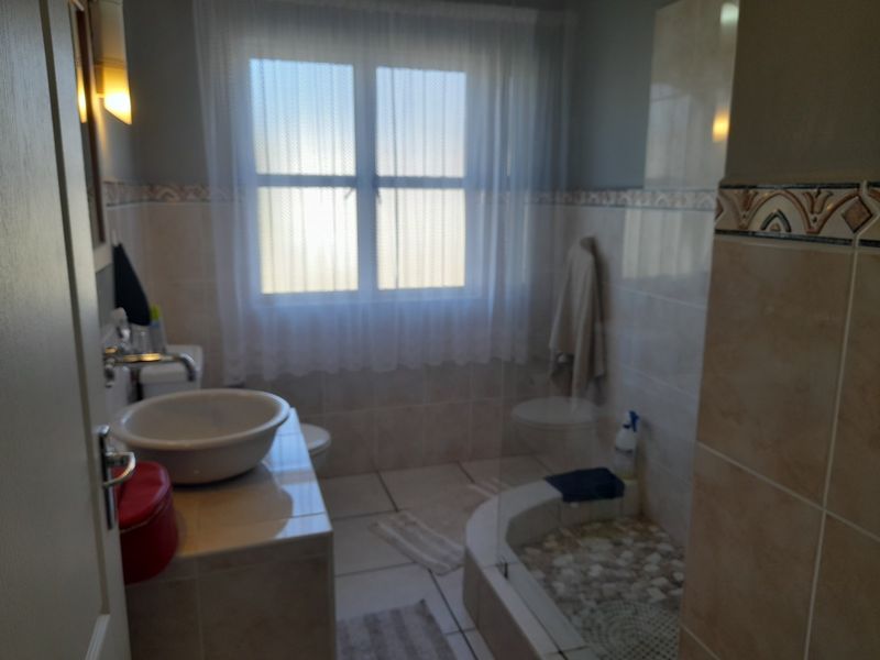 A functional bathroom featuring a vessel sink on a tiled vanity, a walk-in shower with a pebble floor, and neutral wall tiling.