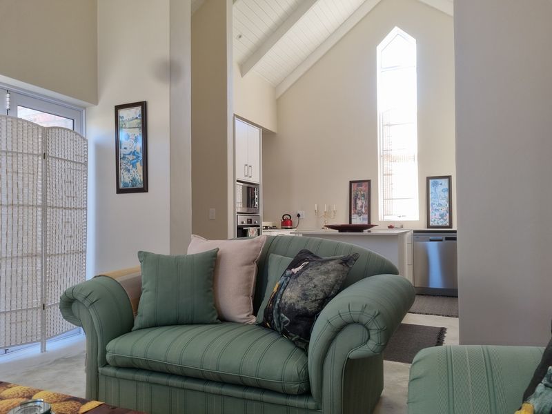 Spacious open-plan living area featuring a high vaulted ceiling, tall feature window, and a modern kitchen with integrated appliances.