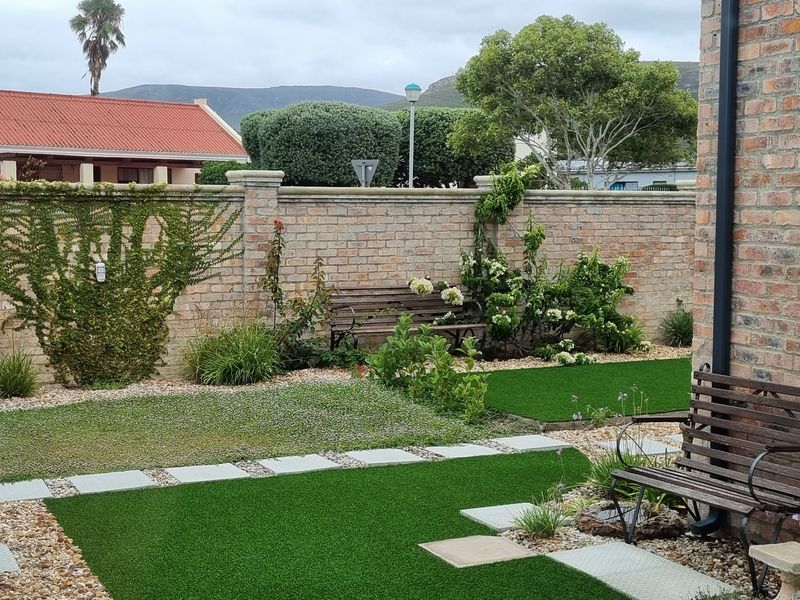 A well-maintained garden featuring artificial turf, stone paver pathways, gravel landscaping, and a sturdy brick boundary wall.