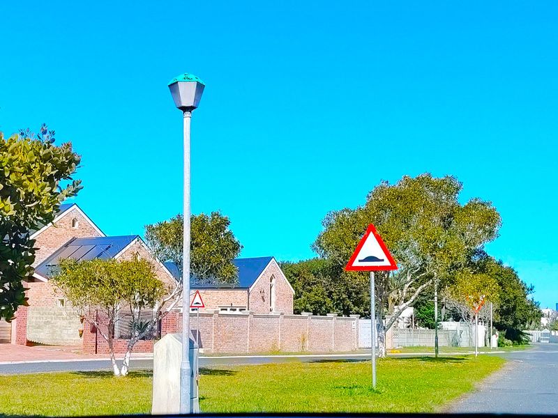 A clear street view showing the residential neighbourhood approach with brick boundary walls, solar panels on the roof, and a street lamp.