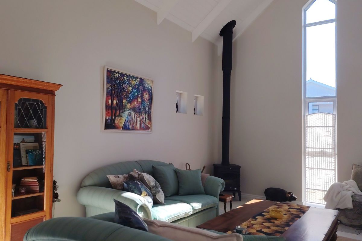Spacious living room featuring a high vaulted ceiling with exposed rafters, a tall feature window, and a black freestanding fireplace.