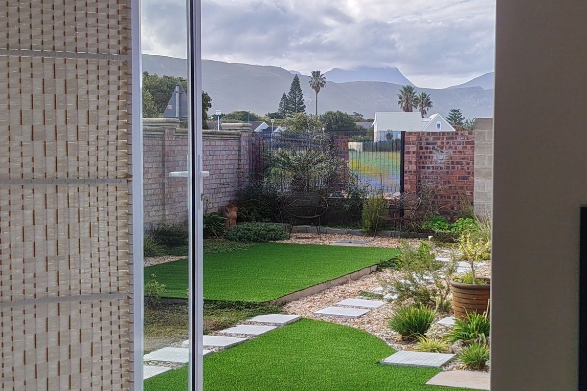 A view of a landscaped rear garden featuring artificial lawn, stone pathways, and a brick boundary wall, framed by a sliding glass door.