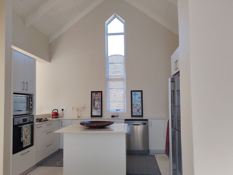 Modern kitchen featuring a high vaulted ceiling, central island, built-in appliances, and a striking gabled window that provides ample natural light.