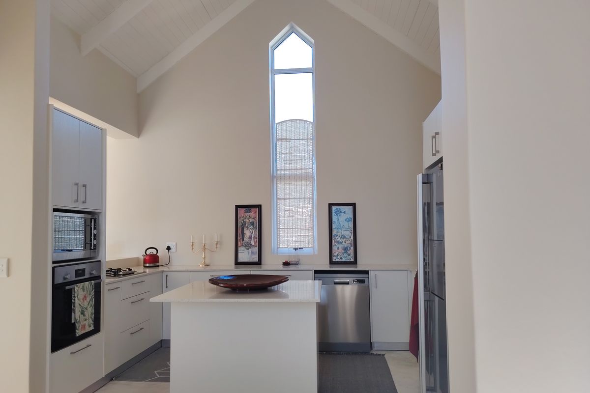 Modern kitchen featuring a high vaulted ceiling, central island, built-in appliances, and a striking gabled window that provides ample natural light.