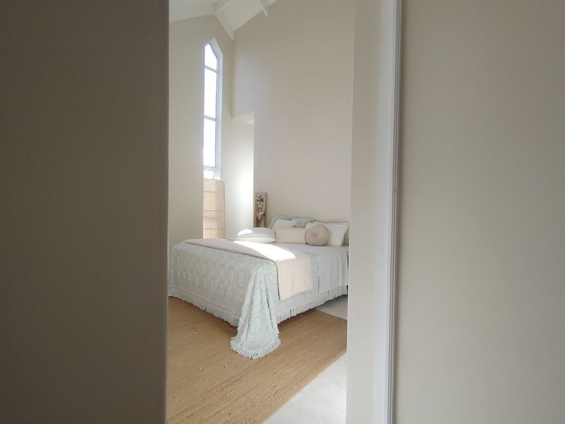 A bright bedroom featuring a high vaulted ceiling and a tall, elegant arched window that allows for ample natural light.