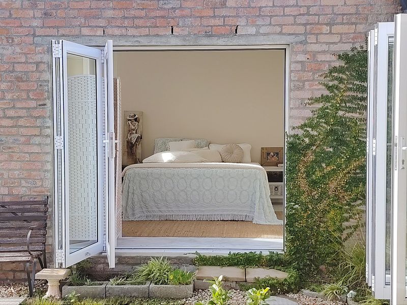 A view into a bedroom through open white bi-fold doors, featuring an exposed brick exterior wall and a small garden threshold.