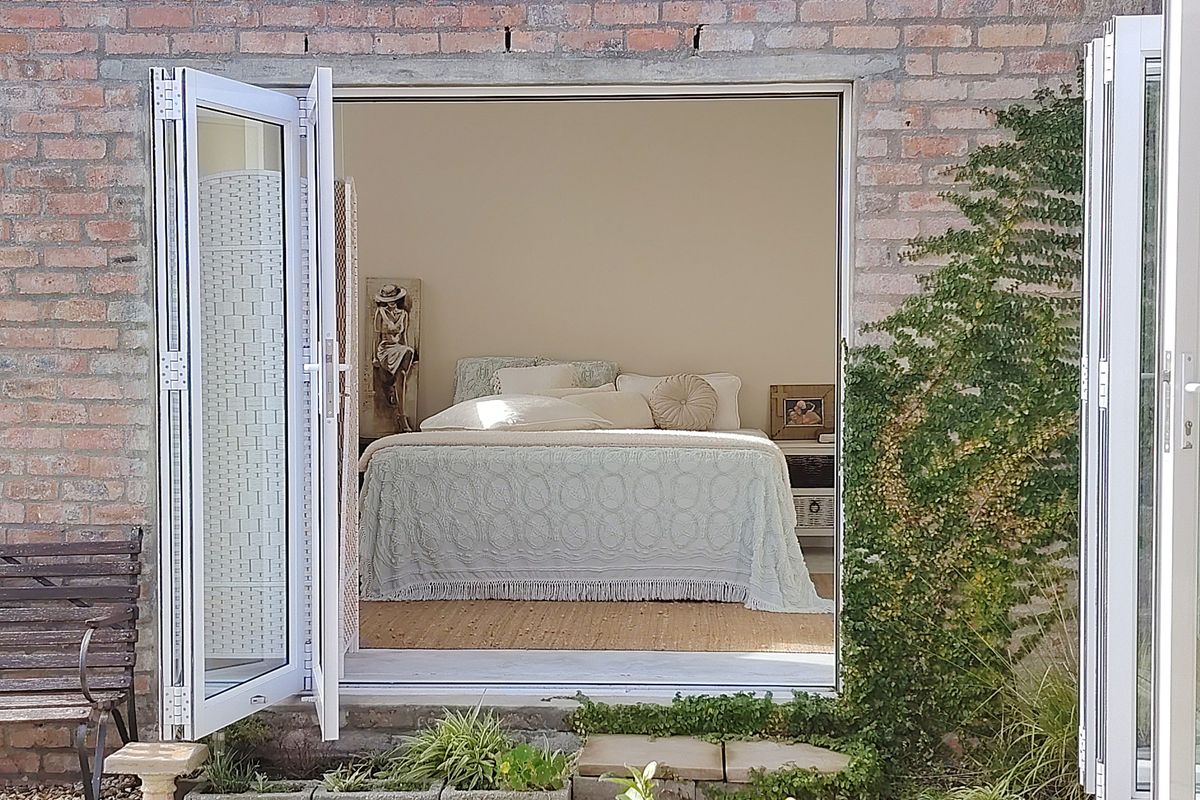 A view into a bedroom through open white bi-fold doors, featuring an exposed brick exterior wall and a small garden threshold.