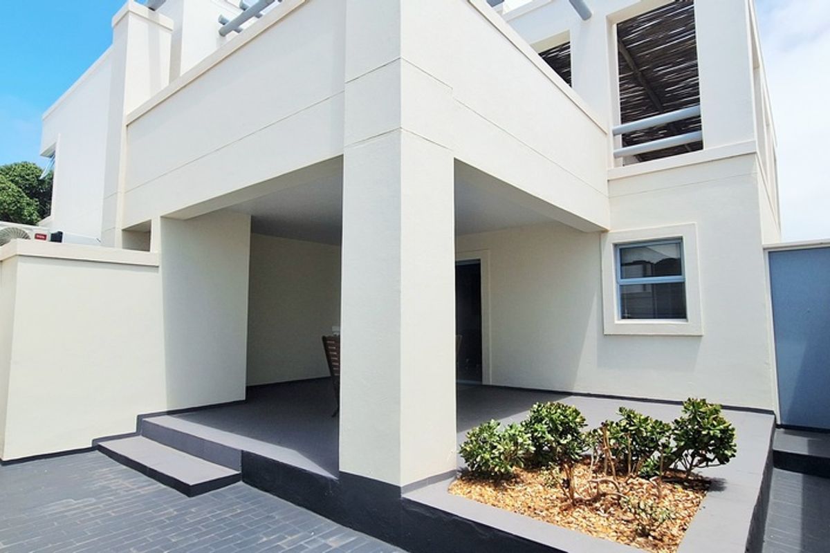 A well-maintained rear exterior view featuring a covered patio, paved courtyard area, and a raised garden bed with a balcony above.