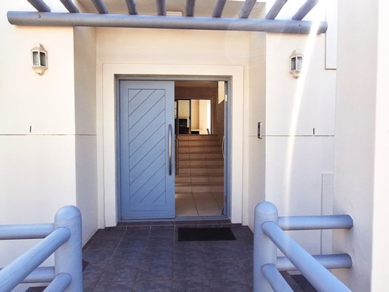 A welcoming front entrance featuring a blue diagonal panel door, a timber pergola overhead, and tiled porch area with matching timber handrails.