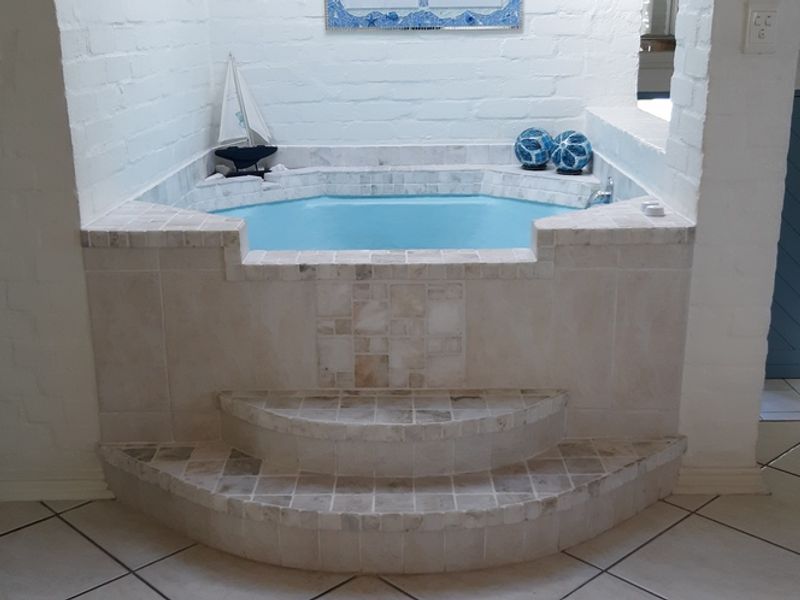 A unique bathroom featuring a built-in sunken bathtub with tiled steps and a stainless steel handrail, set against painted brick walls.