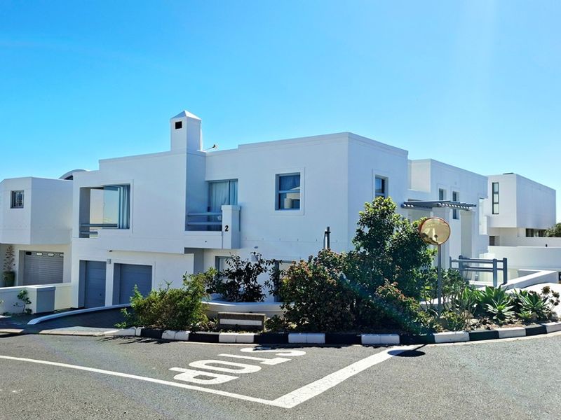 A modern white multi-level residential property featuring a double garage, balcony, and chimney, situated on a corner lot with a paved driveway.