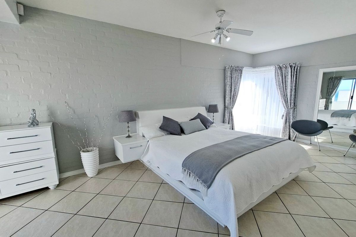 Spacious bedroom featuring neutral painted brick walls, tiled flooring, a ceiling fan, and a sliding glass door providing natural light.