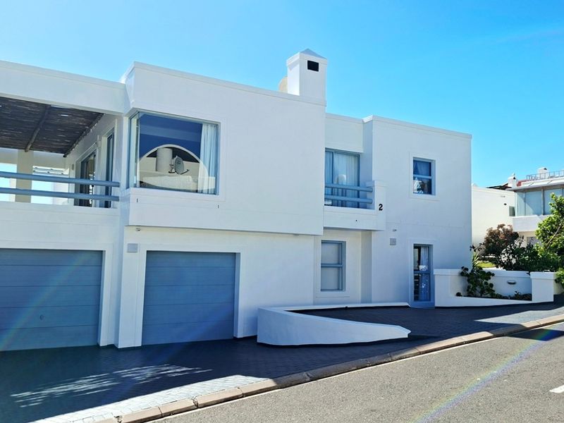 Modern two-story residential facade featuring a double garage, upper-level balcony, and clean white exterior finishes with blue accents.